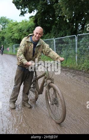 Keith Danford viaggiando in bicicletta attraverso un fangoso sito di Glastonbury. Da una serie di foto che mostrano i festeggiatori che arrivano il primo giorno aperto al pubblico a Glastonbury 2016 su Worthy Farm sotto la pioggia Foto Stock