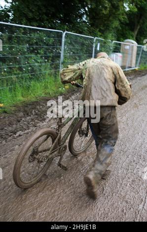 Keith Danford viaggiando in bicicletta attraverso un fangoso sito di Glastonbury. Da una serie di foto che mostrano i festeggiatori che arrivano il primo giorno aperto al pubblico a Glastonbury 2016 su Worthy Farm sotto la pioggia Foto Stock