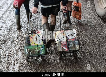 Festivalgoers in wellies arrivo a Glastonbury con birra e vino su un carrello. Le persone che arrivano il primo giorno sono aperte al pubblico a Glastonbury 2016 in Worthy Farm sotto la pioggia Foto Stock