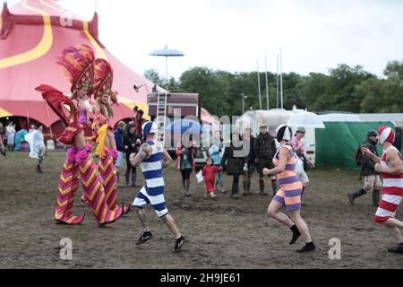 Gli artisti che si esibiscono su palafitte che si muovono attraverso il sito mentre gli appassionati di jogging in costume vecchio stile passano nella direzione opposta al Glastonbury 2016 Festival on Worthy Farm di Somerset Foto Stock