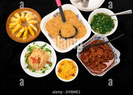 Menu ricco su sfondo nero. Zuppa di piselli, manzo al forno, riso, spaghetti, spinaci stufati e ananas crudo in ciotola o piatto. Foto Stock