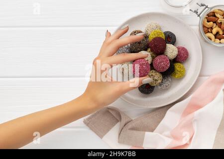 Colorate caramelle vegane palle di energia su un piatto con mano di womans su bianco Foto Stock