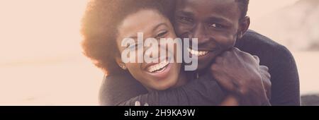 Banner ritratto di nero giovane coppia sorriso e divertirsi insieme in amicizia o rapporto. Uomo abbraccio donna felice all'aperto Foto Stock