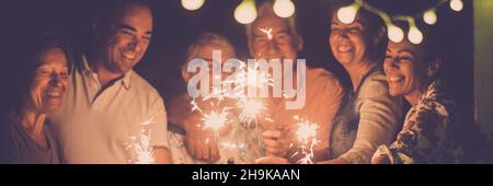 Gruppo di persone festeggiano con scintilla in amicizia. La famiglia con uomini e donne si divertono nella notte festeggiando l'anno nuovo o compleanno in testa banner Foto Stock