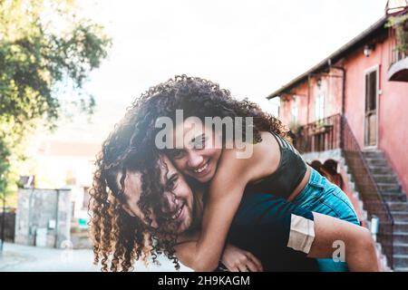 Bella giovane coppia multietnica in stile piggyback - curly ragazza sudamericana in amore si erge sul retro del suo ragazzo caucasico Foto Stock