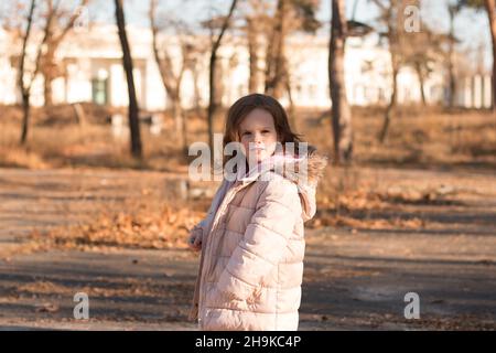 Una ragazza solitario triste in una giacca con un morbido cappuccio si gira e guarda di lato. Bambino in abiti caldi in un parco freddo autunno Foto Stock