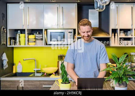 Ritratto di un giovane imprenditore di successo che lavora da casa a casa accogliente tavolo da cucina utilizzando computer portatile fare lavoro facendo chiamata online incontrare Foto Stock