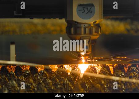 La fresa laser contemporanea incuote sottili lamiere con scintille brillanti in officina scura di impianti di produzione moderni, closeup estremo Foto Stock