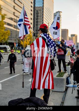 SEUL, COREA - 16 NOVEMBRE 2019: Un anonimo uomo coreano avvolto in una bandiera americana protesta contro le politiche del presidente Moon Jai-in durante un Foto Stock