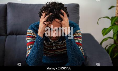 Bel modello maschile si sente stanco dopo il lavoro. Uomo maturo che tiene la fronte mentre ha mal di testa mentre si siede sul divano di casa. Dolore sgradevole. Foto Stock