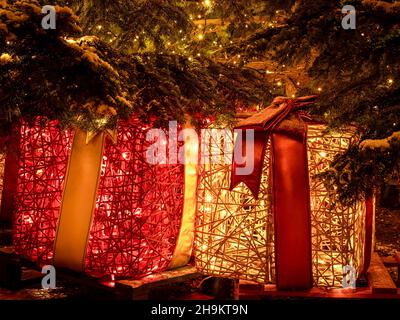 Scatole regalo sotto l'albero di Natale ricoperte di neve e decorate con luci. Foto Stock