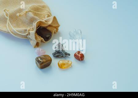 Vista dall'alto della piccola borsa aperta minimalista con cristalli semi-preziosi curativi su sfondo blu Foto Stock