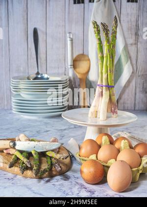 Rustica autunno ancora vita. Asparagi di forma diversa con uova, fondo in legno bianco con piatti e utensili da cucina. Messa a fuoco selettiva. Foto Stock