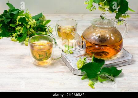 Teiera e due tazze di tè con un tiglio su un tavolo di legno. Tè healing. Foto Stock