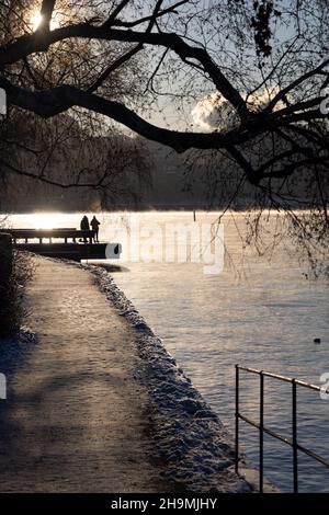 Persone che camminano su un percorso a piedi nella baia di Stoccolma in una gelida giornata invernale con acqua fumante, albero di betulla di fronte e accogliente luce solare. Ora invernale Foto Stock