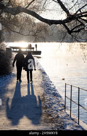 Persone che camminano su un percorso a piedi nella baia di Stoccolma in una gelida giornata invernale con acqua fumante, albero di betulla di fronte e accogliente luce solare. Ora invernale Foto Stock