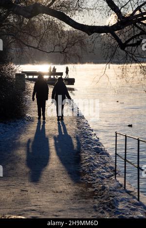 Persone che camminano su un percorso a piedi nella baia di Stoccolma in una gelida giornata invernale con acqua fumante, albero di betulla di fronte e accogliente luce solare. Ora invernale Foto Stock