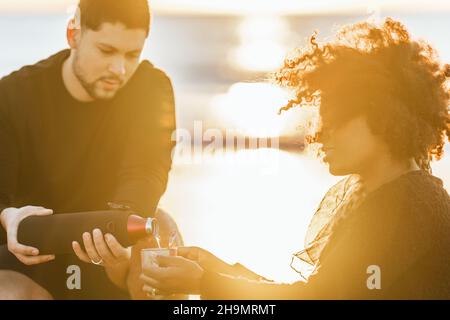 Tramonto che illumina un uomo che serve il tè a una donna seduta sulla spiaggia Foto Stock