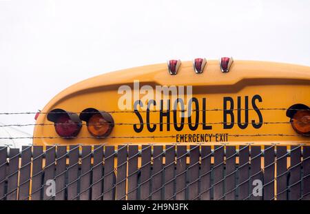 Scuolabus parcheggiato dietro un recintato in zona con filo spinato Foto Stock