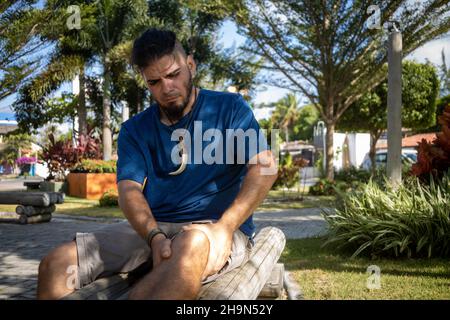 Giovane hippie che guarda l'uomo che tiene il ginocchio con entrambe le mani per alleviare il dolore. Foto Stock