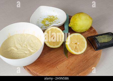 Limone siciliano tagliato a metà accanto ad una pentola di ganache di cioccolato bianco, scorza di limone e una grattugia metallica. Foto Stock