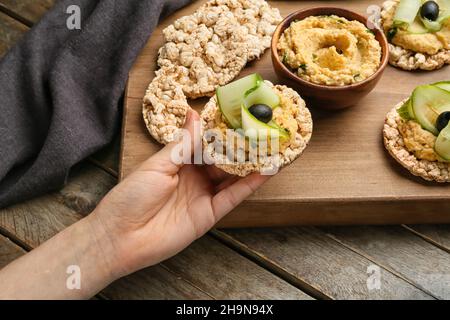 Donna che tiene cracker di riso con delizioso hummus su sfondo di legno Foto Stock