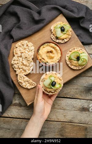 Donna che tiene cracker di riso con delizioso hummus su sfondo di legno Foto Stock