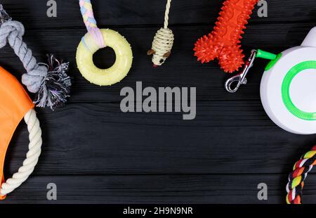 Accessori diversi per cani e gatti: Giocattolo per mouse, palla, pettine, guinzaglio, colletto, giocattoli e ciotola con ossa su sfondo di legno nero. Animali domestici cura e rout Foto Stock