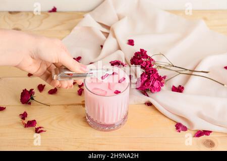 Donna che aggiunge ghiaccio al gustoso latte di rosa in vetro sul tavolo Foto Stock