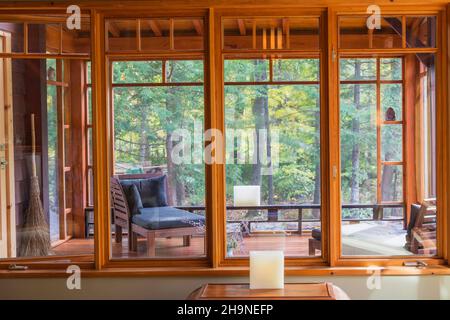 Piccolo tavolo indonesiano in legno di teak con vista dell'ufficio domestico attraverso le finestre nella sala da pranzo in stile giapponese all'interno di una casa con struttura in legno di design open-concept. Foto Stock