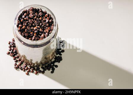 Getto in alto di chicchi di caffè torrefatti in un'ombra di colata del vaso di vetro Foto Stock