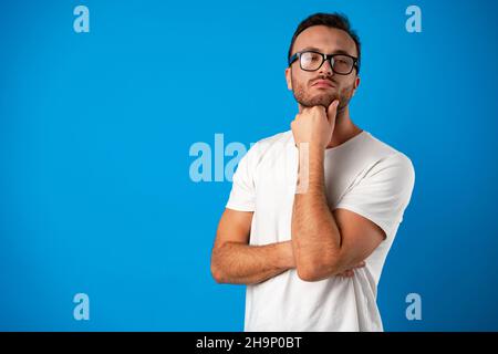 Pensieroso bel maschio indossare occhiali su sfondo blu Foto Stock