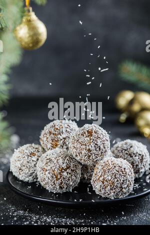 Dolce di Natale vegano crudo palle di energia sana con farinata d'avena, seme di chia, fiocchi di cocco, frutta secca. Decorata con rami di abete Foto Stock