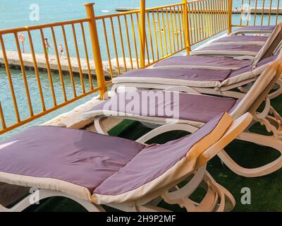 Sedie a sdraio vuote con materassi sull'aerario per rilassarsi sulla spiaggia di un hotel o resort, sullo sfondo del mare. Foto Stock