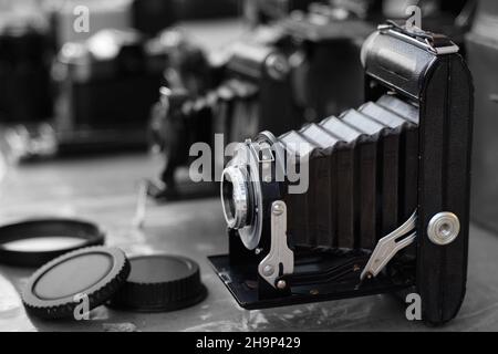 Mantici di estensione di una vecchia fotocamera di pellicola di foto pieghevole e altri attrezzi in background, mercato delle pulci di Yerevan. Messa a fuoco selettiva sul bordo dell'obiettivo Foto Stock