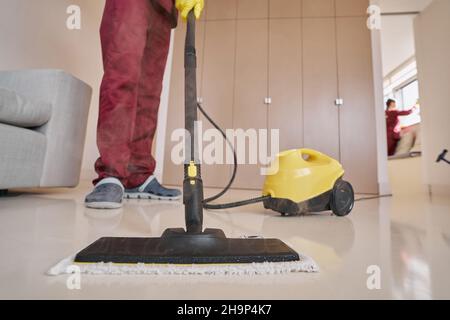 Housecleaner in guanti di gomma che applicano attrezzature per la pulizia a vapore Foto Stock