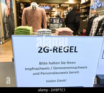 Magonza, Germania. 07th Dic 2021. All'entrata del negozio di moda Engbers nel centro di Mainz, c'è un cartello che dice '2G regola. Si prega di tenere a portata di mano la prova della vaccinazione/genetica e l'ID. Grazie!". La città di Magonza ha modificato la sua ordinanza di Corona. Secondo questo, le persone con un braccialetto 2G dal mercato di Natale possono anche andare a fare shopping nei negozi di Mainz. (A dpa: 'Shopping di Natale con prova di vaccinazione fa registrare i contanti squillare meno spesso') accreditamento: Arne Dedert/dpa/Alamy Live News Foto Stock