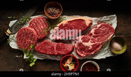 Composizione di testa di bistecche di manzo crudo assortite ribeye e di sirloin con cotolette poste su carta sbriciolata Foto Stock