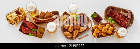 Vista dall'alto di piatti con deliziosi spuntini posizionati vicino a bicchieri di birra sulla superficie bianca in studio Foto Stock