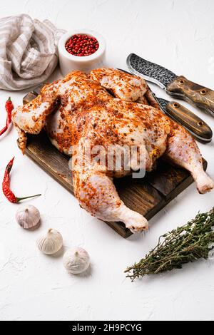 Tabaka di pollo crudo pronto per la cottura con ingredienti impostati, su sfondo bianco tavola di pietra Foto Stock
