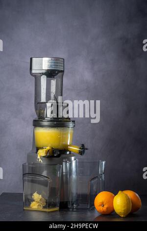 due arance e un limone davanti a un estrattore per succhi. il succo scorre in un contenitore Foto Stock