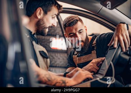 Due meccanici moderni che eseguono la diagnostica in auto. Concetto di lavoro. Foto Stock