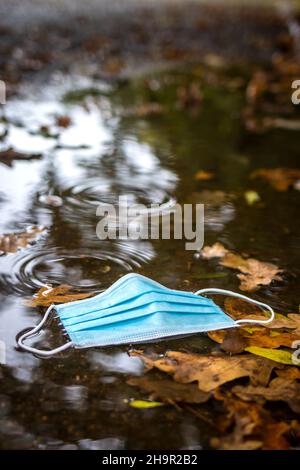 Usato maschera in puddle su strada. Problemi di inquinamento durante la pandemia di covid-19. Nuova normalità in città Foto Stock