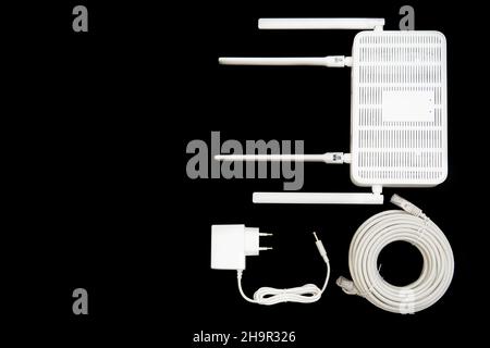 Vista dall'alto di un router Wi-Fi 6 dual band con un adattatore di alimentazione e un rotolo di cavo ethernet isolato in nero. Foto Stock