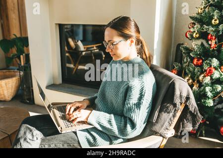 Lavoro a casa, videoconferenza, videochiamata per riunioni online, riunioni virtuali, apprendimento a distanza. Una donna d'affari in abiti casual conduce una videochiamata, si impegna in e-mail, comunica online con i colleghi, invia e risponde alle e-mail, sviluppa software mentre si siede a casa sul divano. Una donna intelligente lavora da remoto. Foto Stock