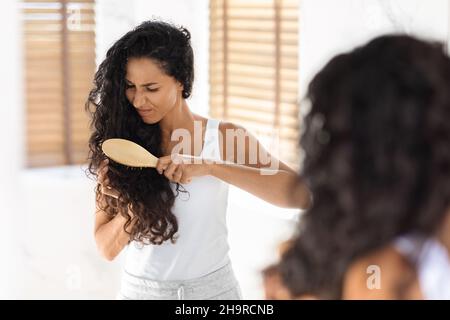 Giovane donna Brunette irritata da capelli aggrovigliati, utilizzando Bamboo Brush in bagno Foto Stock