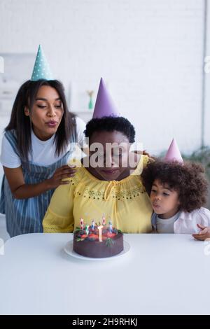 le donne e la bambina afroamericane in cappellini di festa che soffiano le  candele sulla torta di compleanno Foto stock - Alamy