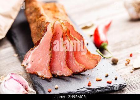 Tenderloin di maiale stagionato secco sul piano di servizio ardesia con aglio e peperoncino. Lonzino, antipasto con filetto a jerky su sfondo di legno. Foto Stock