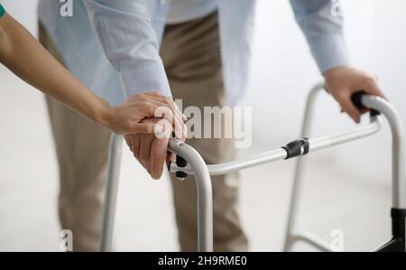 Uomo anziano irriconoscibile che usa aiuto per camminare, giovane donna che lo sostiene e lo aiuta a casa, vista closeup Foto Stock