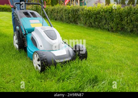 Un uomo che rasa erba con un tosaerba in giardino in una giornata di sole. Un rasaerba sul prato, un primo piano. Foto Stock